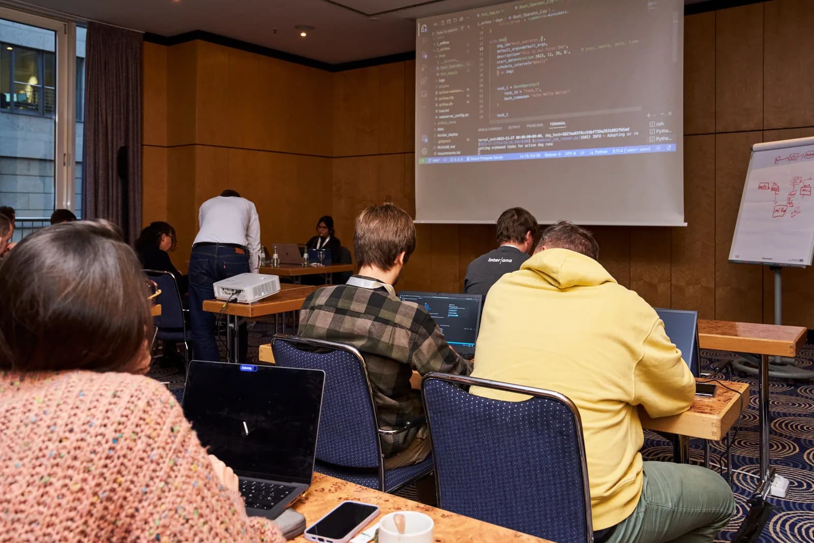 Over-the-shoulder view of the same workshop, attendees following along in their own editors while a terminal runs at the front of the room.