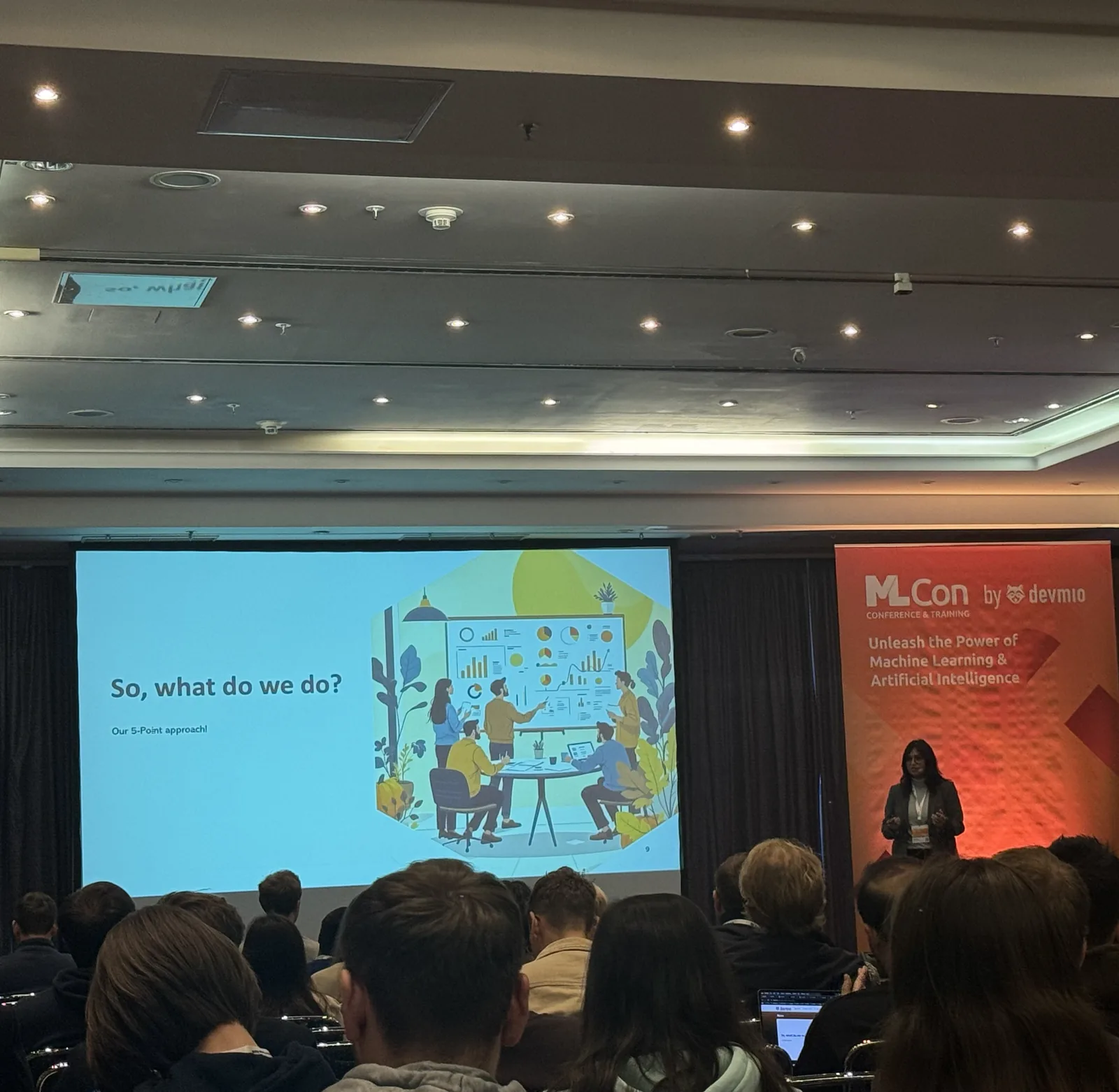 Saumya presenting to a seated audience beside an ML Conference banner, with a slide reading "So, what do we do?" projected on screen.