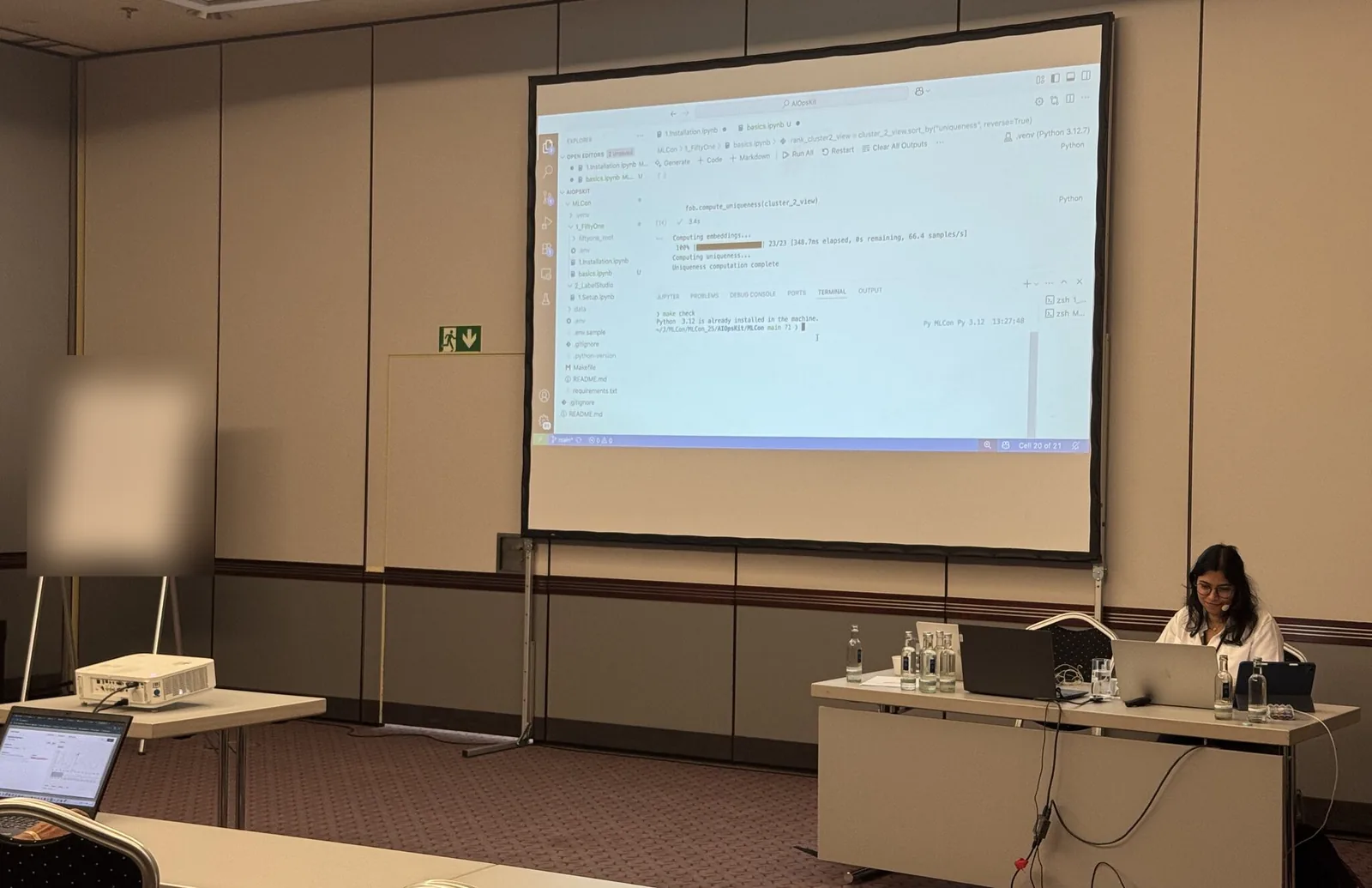 Saumya running a live coding demo from the front of a workshop room, a notebook and terminal projected on the screen behind her.