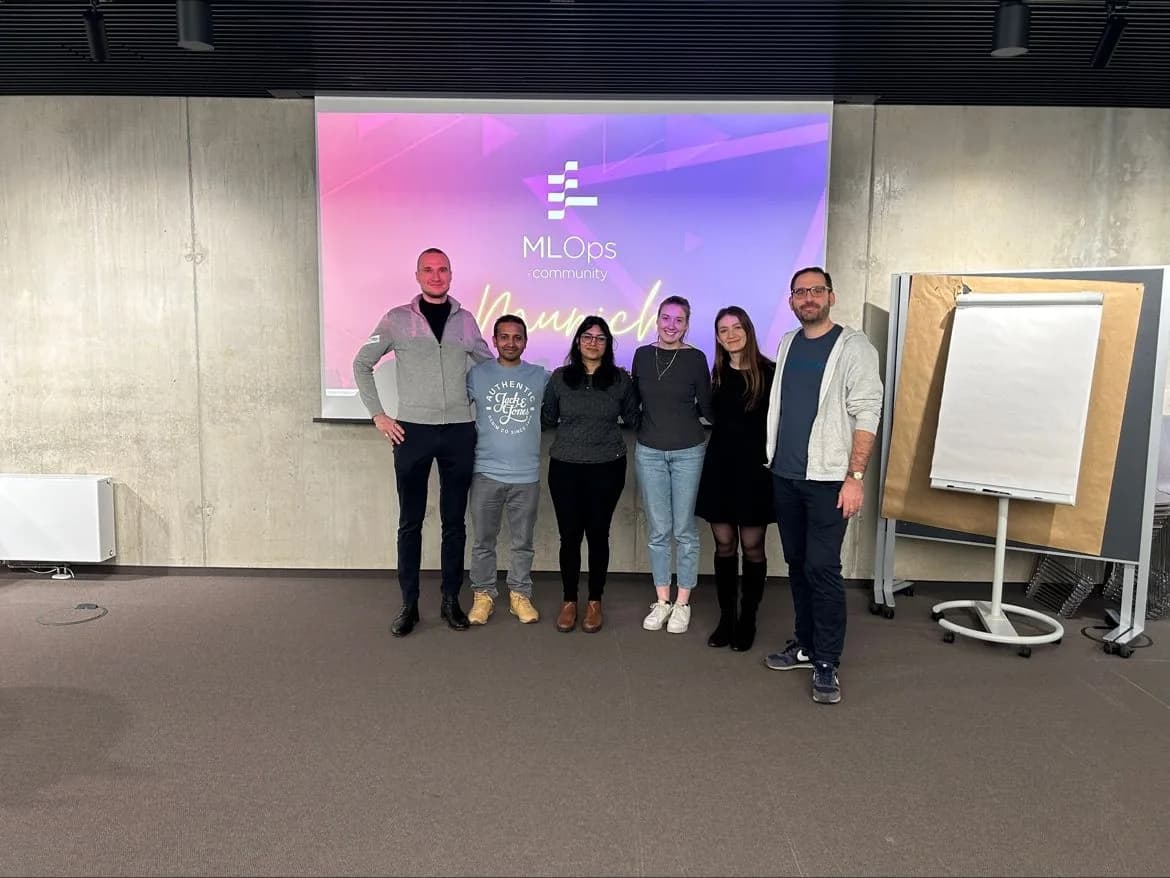 Saumya with five fellow speakers and organisers in front of the MLOps Community Munich title slide.